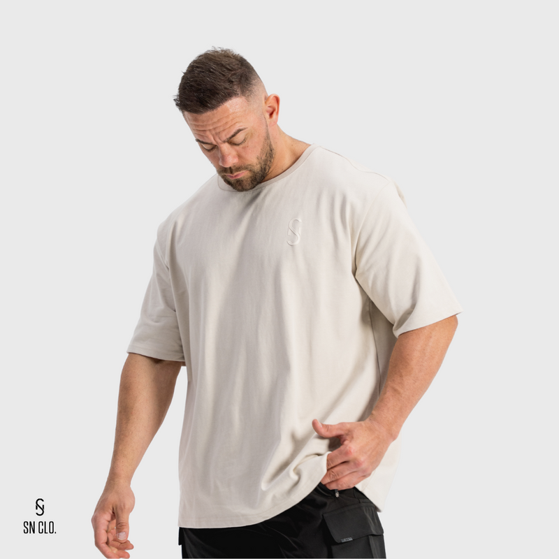 Man wearing a beige t-shirt with a SN Clo logo on a white background
